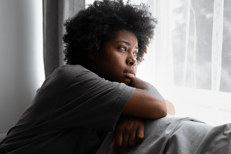 Person sitting by a bright window, looking out thoughtfully