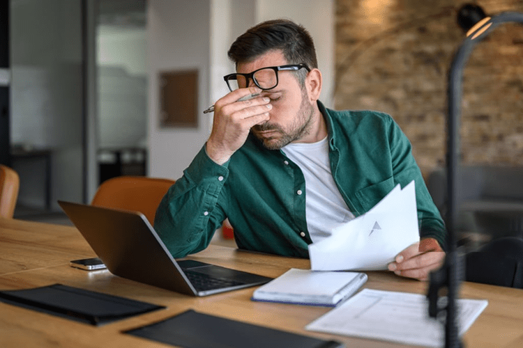 Person at a desk with a laptop, pinching the bridge of their nose