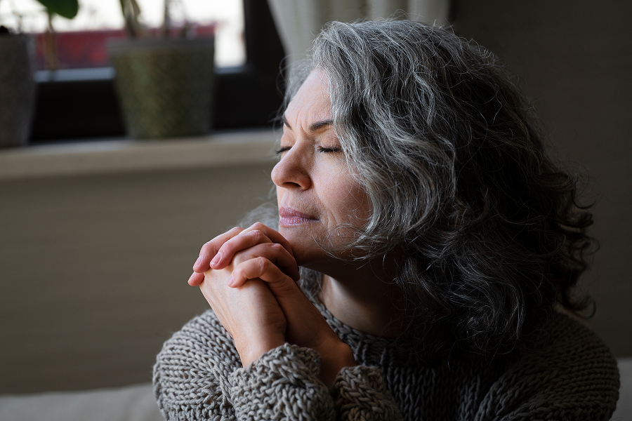 Older woman with her eyes closed and hands clasped in quiet reflection