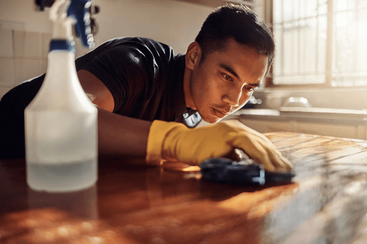 Young man in rubber gloves scrubbing a table